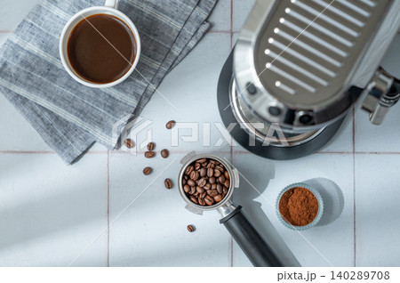 A flat lay of a cup of black coffee, a portafilter with roasted beans and an espresso machine A flat lay of a cup of black coffee, a portafilter with roasted beans and an espresso machine 140289708