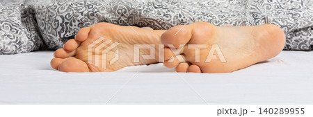 A man enjoys his time relaxing on a bed. His feet can be seen sticking out from under a gray blanket. It looks like a comfortable setting at home or in a hotel, banner A man enjoys his time relaxing on a bed. His feet can be seen sticking out from under a gray blanket. It looks like a comfortable setting at home or in a hotel, banner 140289955