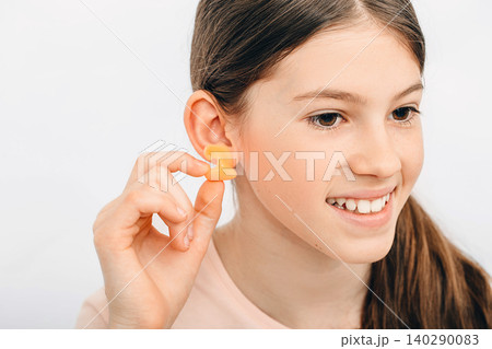 Individual earplugs for children. Girl holding individual earplug near ear, close-up. Individual earplugs for children. Girl holding individual earplug near ear, close-up. 140290083
