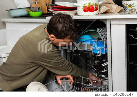 A man is at work in the kitchen, pouring salt into a dishwasher as he prepares to wash dirty dishes. He is focused on the task at hand while organizing the appliances A man is at work in the kitchen, pouring salt into a dishwasher as he prepares to wash dirty dishes. He is focused on the task at hand while organizing the appliances 140290147