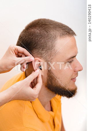 Man patient with Intra-ear hearing aid, close-up inside the male ear. Hearing solution, audiologist inserting hearing aid to patient Man patient with Intra-ear hearing aid, close-up inside the male ear. Hearing solution, audiologist inserting hearing aid to patient 140290418