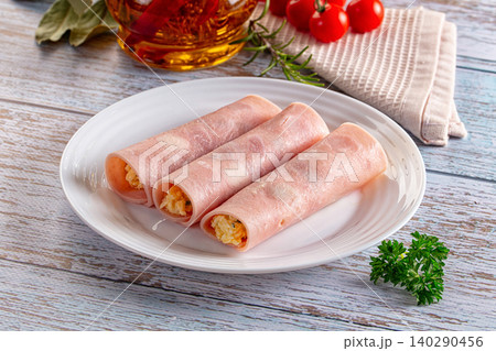 Ham rolls with savory filling on white plate with herbs and tomatoes 140290456