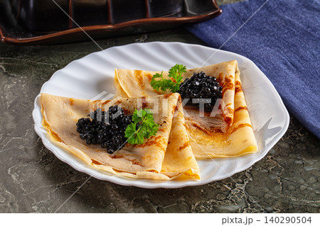 Delicate pancakes topped with black caviar and fresh parsley on a white plate Delicate pancakes topped with black caviar and fresh parsley on a white plate 140290504