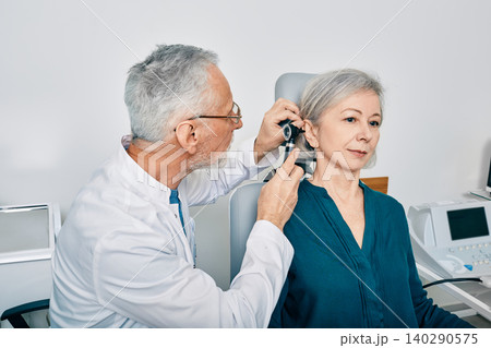 Otolaryngologist doctor checking senior woman's ear using otoscope or auriscope at hearing center. Audiology 140290575