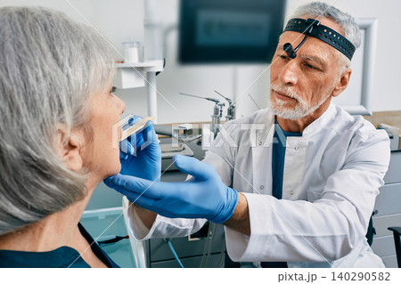 Doctor using inspection spatula examines senior woman throat. ENT doctor consultation, throat exam Doctor using inspection spatula examines senior woman throat. ENT doctor consultation, throat exam 140290582