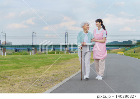 土手を散歩する日本人シニア女性と若い女性介護士 土手を散歩する日本人シニア女性と若い女性介護士 140290827