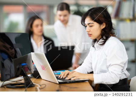 In office, young Asian woman is working on laptop as part of group of colleagues 140291231