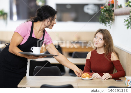 Latin female waiter serves cafes customers and places order on table for girl 140291358
