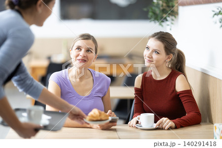 Friendly waitress brought croissants and coffee to female customers Friendly waitress brought croissants and coffee to female customers 140291418