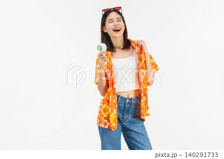Happy smiling young Asian woman in summer wearing floral shirt holding fan to cool herself with suffers from too hot weather in white background 140291733