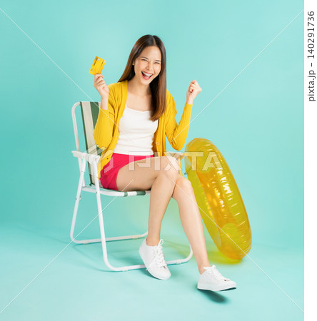 Happy smiling young Asian woman sit in deckchair and rubber ring in yellow color with holding credit card on blue background 140291736