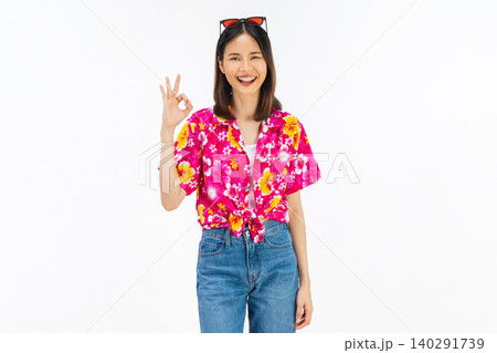 Smiling young Asian woman showing OK hand gesture in summer floral shirt isolated on white studio background. Smiling young Asian woman showing OK hand gesture in summer floral shirt isolated on white studio background. 140291739
