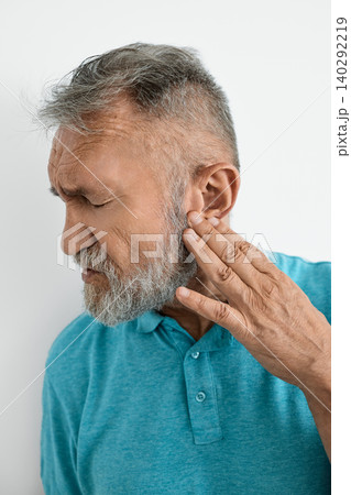 Senior man struggling with hearing aspects, gently touching his ear as discomfort shows on his face 140292219