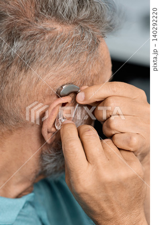 Grey-haired senior man with hearing impairment using hearing aid. Hearing solutions for deafness people Grey-haired senior man with hearing impairment using hearing aid. Hearing solutions for deafness people 140292220