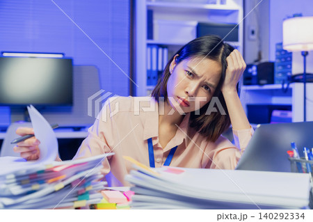 Stressed young Asian office worker feeling overwhelmed with paperwork and workload while working on laptop in office Stressed young Asian office worker feeling overwhelmed with paperwork and workload while working on laptop in office 140292334
