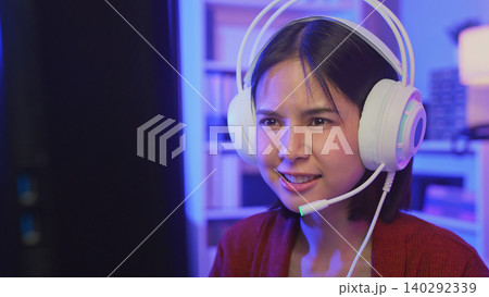 Excited young Asian girl playing online computer game with headset and microphone at home, esports and live streaming concept. 140292339
