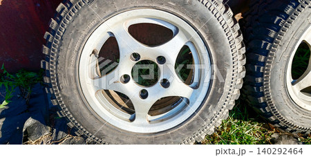 Silver alloy wheel with five spokes and black tire resting on grass beside another tire, showcasing detailed design and texture in natural outdoor setting 140292464