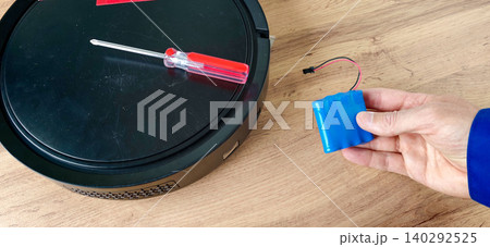 Robot vacuum cleaner battery replacement process with a screwdriver and new battery on a wooden surface, showcasing the repair tools and components involved Robot vacuum cleaner battery replacement process with a screwdriver and new battery on a wooden surface, showcasing the repair tools and components involved 140292525