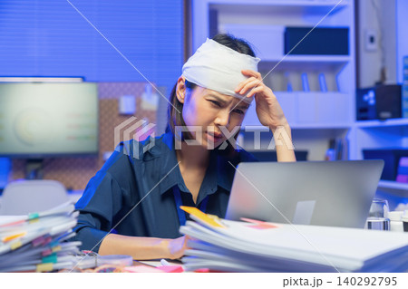 Injured young Asian office worker wearing head bandage while working on laptop in office, health and work pressure concept. Injured young Asian office worker wearing head bandage while working on laptop in office, health and work pressure concept. 140292795