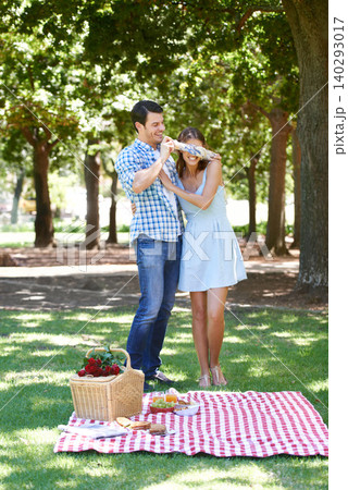 Love, picnic and surprise with couple in park for romance, bonding and summer vacation. Happiness, commitment and relax with man and blindfold woman in nature for date, support and relationship 140293017