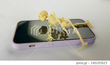 Small skeleton figurine lying on a smartphone screen, showcasing the concept of gadget addiction with a playful and humorous visual representation Small skeleton figurine lying on a smartphone screen, showcasing the concept of gadget addiction with a playful and humorous visual representation 140293025