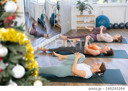 Women practice yoga during the New Year celebration in the studio, lie on the mat, perform stretching in Ardha Pavanmuktasana pose Women practice yoga during the New Year celebration in the studio, lie on the mat, perform stretching in Ardha Pavanmuktasana pose 140293264
