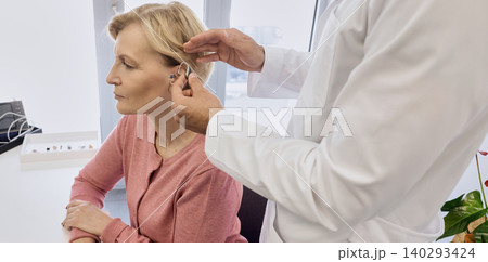 Audiologist putting hearing aid on mature woman's ear at audiology center, close-up, side view. Deafness treatment, hearing solutions 140293424