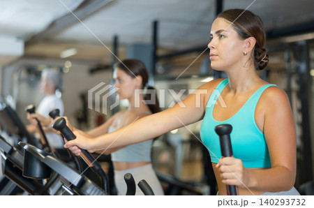 Portrait of sporty woman doing cardio workout on elliptical cross trainer at fitness center Portrait of sporty woman doing cardio workout on elliptical cross trainer at fitness center 140293732