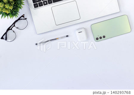 Minimalist workspace with sleek gadgets. Green phone rests beside laptop and mouse. White earbuds and pen add functional touch. Clean desk invites calm, focused productivity Minimalist workspace with sleek gadgets. Green phone rests beside laptop and mouse. White earbuds and pen add functional touch. Clean desk invites calm, focused productivity 140293768