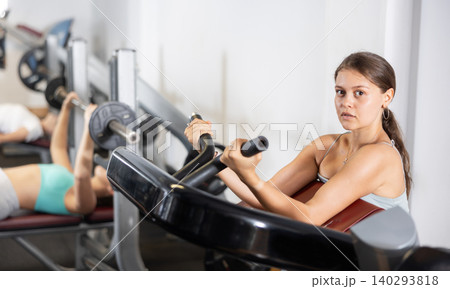 Slender athletic girl work out muscles of arms and shoulders on simulator in gym of fitness club 140293818