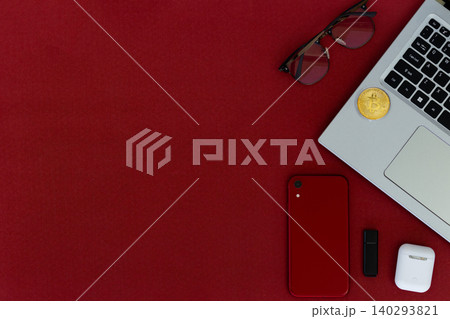 Red surface holds tech and accessories. Laptop, phone, earbuds, and sunglasses rest nearby. Small plant adds green contrast to bold red. Cozy, stylish, modern scene for digital lifestyles Red surface holds tech and accessories. Laptop, phone, earbuds, and sunglasses rest nearby. Small plant adds green contrast to bold red. Cozy, stylish, modern scene for digital lifestyles 140293821
