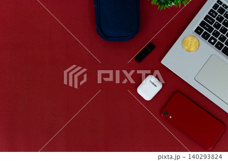 Red surface holds tech and accessories. Laptop, phone, earbuds, and sunglasses rest nearby. Small plant adds green contrast to bold red. Cozy, stylish, modern scene for digital lifestyles Red surface holds tech and accessories. Laptop, phone, earbuds, and sunglasses rest nearby. Small plant adds green contrast to bold red. Cozy, stylish, modern scene for digital lifestyles 140293824
