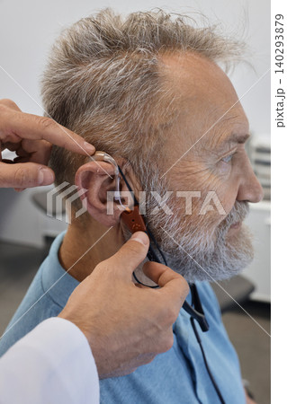 Hearing solutions. Audioprosthetist adjusts senior patient's hearing aids using special equipment, and takes real ear measurements 140293879