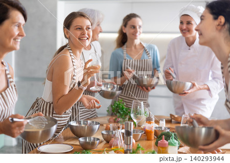 Young woman holding wine and talking to other cooking course members whipping souce in bowls 140293944