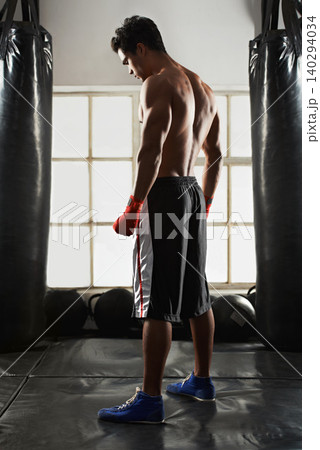 Fitness, man and gloves in gym with punching bag for exercise, sports and training for competition. Male person, back view and boxing with Muay Thai for fighting, performance and skill at club studio 140294034