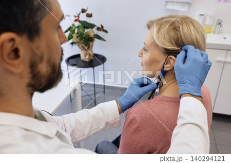 Specialist fine-tunes a hearing aid for a client, ensuring a perfect fit and optimal sound quality. Audiology, hearing treatment Specialist fine-tunes a hearing aid for a client, ensuring a perfect fit and optimal sound quality. Audiology, hearing treatment 140294121