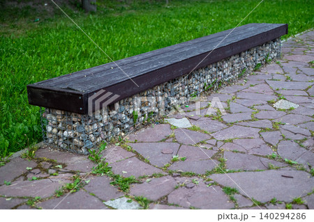 Dark wooden bench rests on a stone base Dark wooden bench rests on a stone base 140294286
