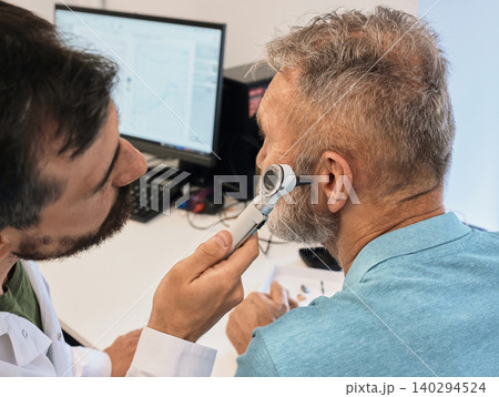 Diagnosis of hearing impairment, check-up, otoscopy. Elderly man while ear test with audiologist with otoscopy at medical office, close-up 140294524