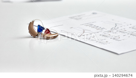 Left and right hearing aids lying on audiologist table near hearing test documents. Hearing check-up concept Left and right hearing aids lying on audiologist table near hearing test documents. Hearing check-up concept 140294674