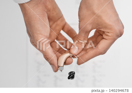Audiologist holding a hearing aid and a battery in her hands, close-up. Hearing clinic. 140294678