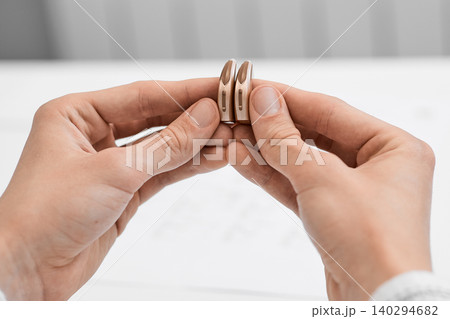 Audiologist carefully examine a pair of sleek hearing aids designed for improved auditory clarity and comfort Audiologist carefully examine a pair of sleek hearing aids designed for improved auditory clarity and comfort 140294682