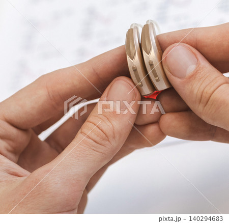 Doctor holds a pair of modern compact hearing aids made individually for audiology clinic patient, close-up 140294683