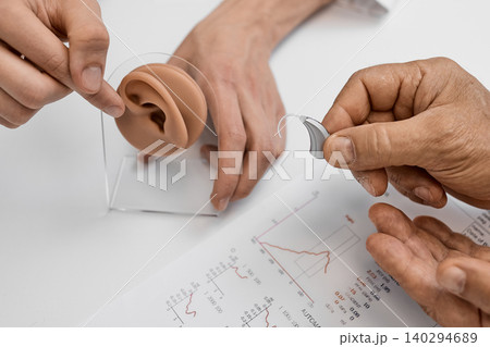 Client learns about hearing aids while examining ear anatomy with a professional at an audiologist office. Hearing solutions 140294689