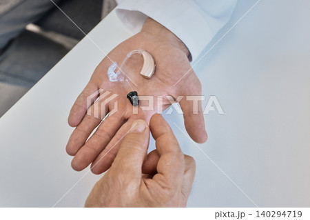 Audiologist holding on hand behind-the-ear and in-the-canal hearing aid for patient to choose from in hearing clinic, close-up, top view Audiologist holding on hand behind-the-ear and in-the-canal hearing aid for patient to choose from in hearing clinic, close-up, top view 140294719