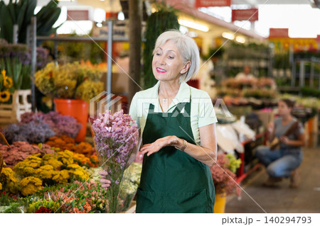 Elderly female florist offering bouquet of limonium in flower shop Elderly female florist offering bouquet of limonium in flower shop 140294793