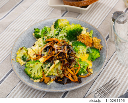 There is stewed broccoli and pickled wild mushrooms chanterelle on plate. 140295196