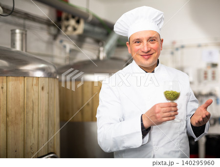 Smiling brewmaster holding glass of pelleted hops in brewery Smiling brewmaster holding glass of pelleted hops in brewery 140295960