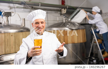 Successful brewmaster holding glass of foamy pale ale Successful brewmaster holding glass of foamy pale ale 140296267