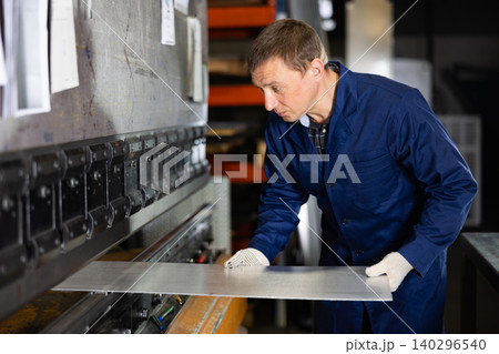 Metallurgical plant - male worker bending sheet of metal on press 140296540
