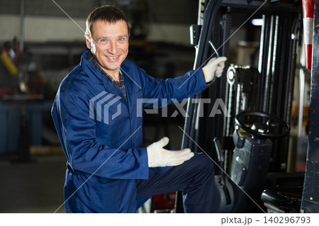 Adult man posing by forklift in workshop Adult man posing by forklift in workshop 140296793